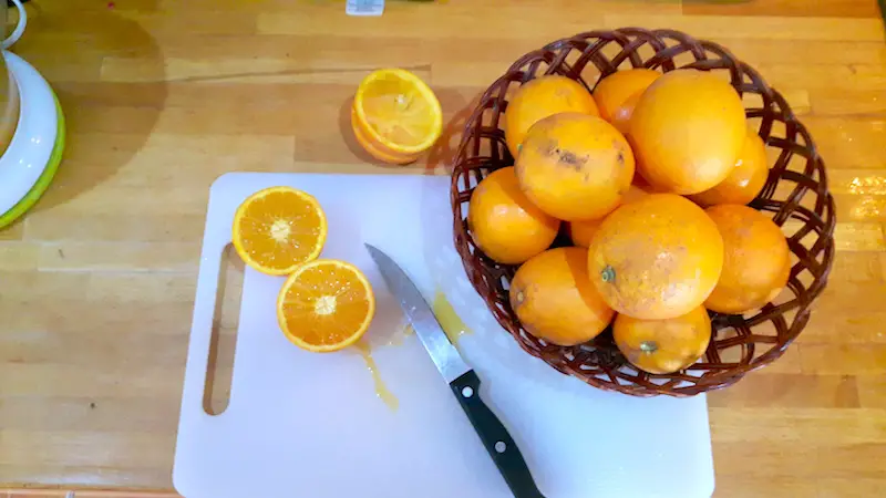 Basket of oranges with one cut in half on a white chopping board.