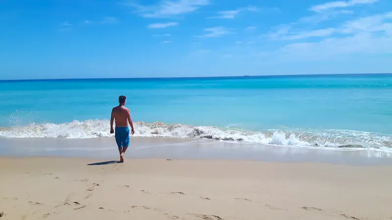 man walking into an incredibly blue sea at Praia do Porto de Mos, Lagos Portugal.