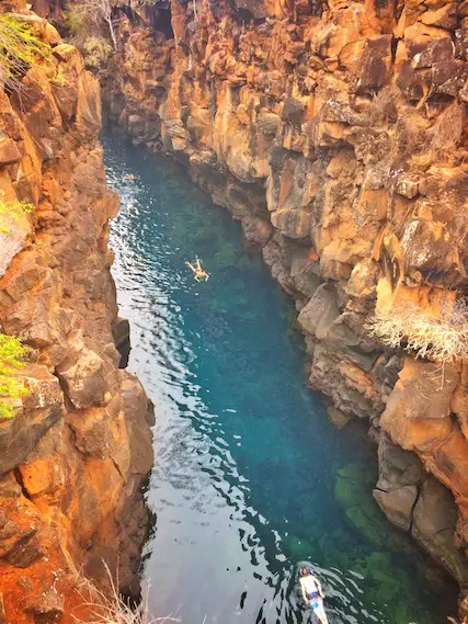 Looking down into a long narrow crack in the rock to see someone swimming in clear water. Las Grietas, Galapagos.