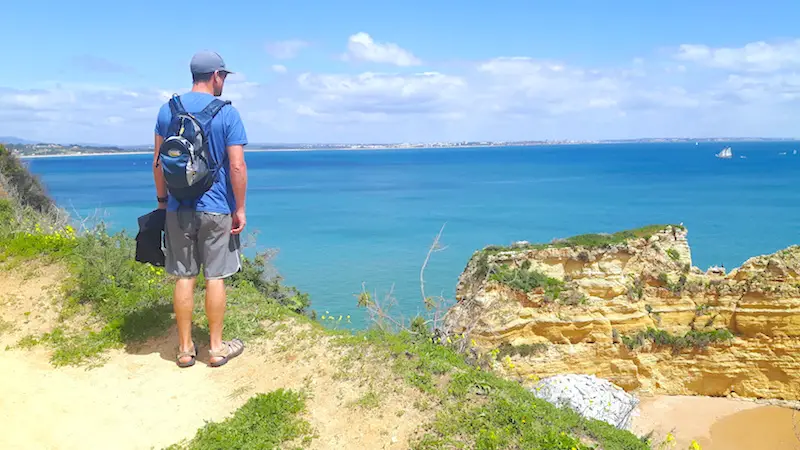 Man standing at the edge of a high cliff looking down to the ocean in Portugal.