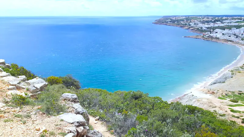 View over cliff to a wide blue bay and small town, Algarve Portugal.