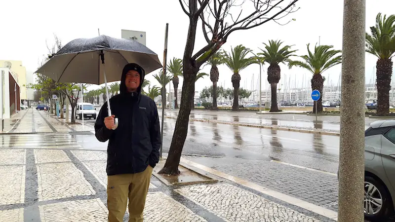 Man on a mosaic sidewalk with an umbrella in the pouring rain in Portugal.