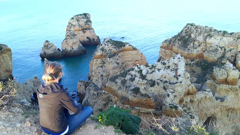 Woman sitting on the edge of a high cliff down to interesting rock formation in the sea at Ponte de Piedade, Portugal.