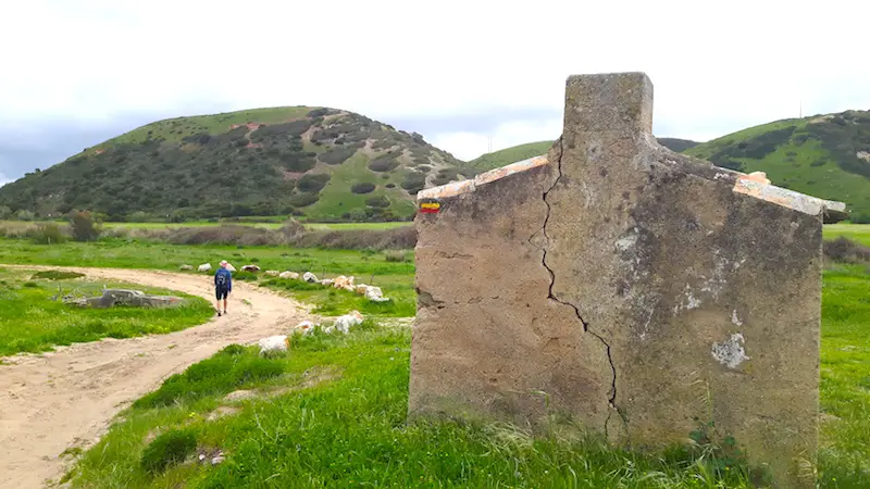 an abandoned building with a hiking trail marking on the side and man walking down the path in Portugal.