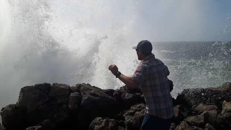 Man running from a huge wave crashing on rocks, Vicentina Portugal