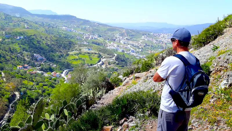 Man standing on a mountainside looking down the valley to Chefchaouen, Morocco.