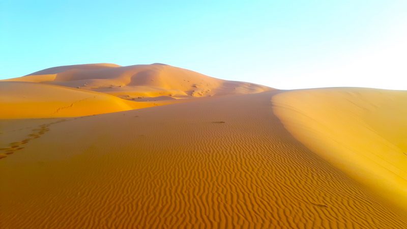 Erg Chebbi sand dunes turn shades of orange at sunset in Sahara Desert Morocco.