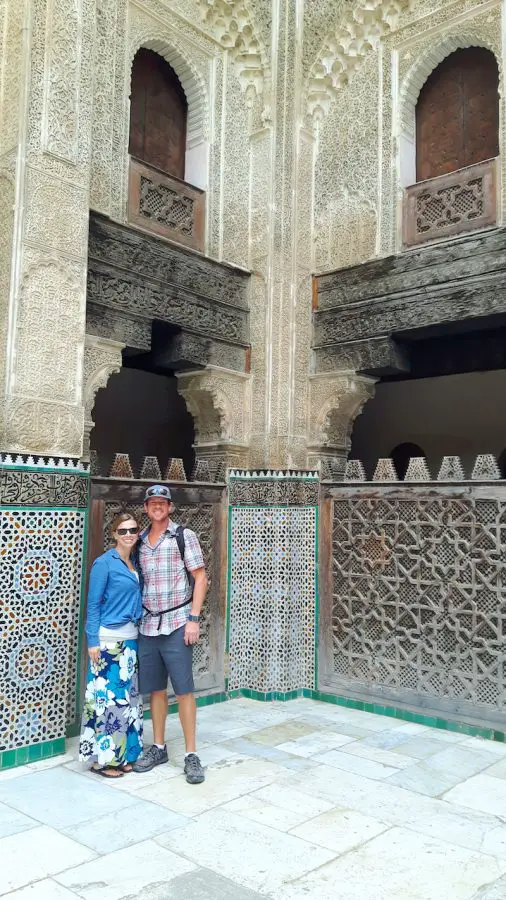 Couple standing inside an intricately carved and tiles mosque in Fes, Morocco.