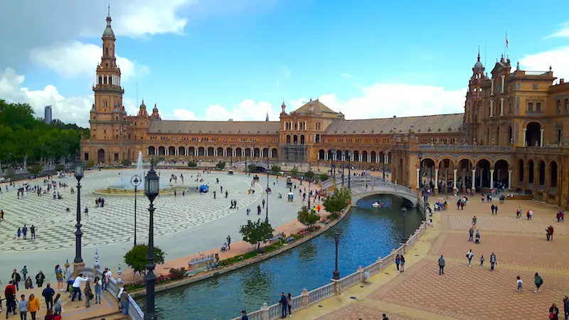 Long, curved building around a central plaza with water features in Seville, Spain.