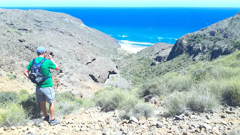 Man looking across a rocky ravine to the bright blue Mediterranean while hiking in Cabo de Gata, Spain.