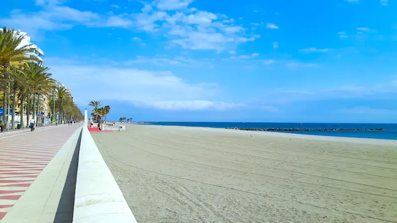 Long empty golden beach with a colourfully tiled promenade running alongside in Almeria Spain.