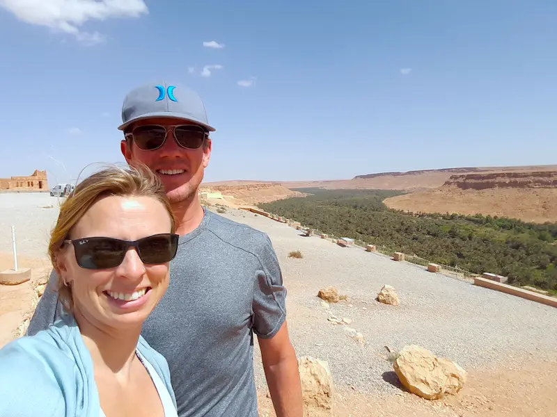 Couple standing in front of green oasis running through a desert valley in Morocco.