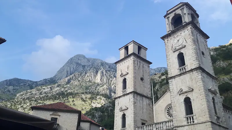 Twin towers of church with tall mountains behind in Kotor, Montenegro.