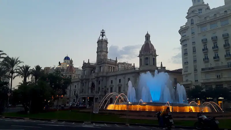 Fountain brightly lit at dusk with grand buildings behind in Valencia, Spain.