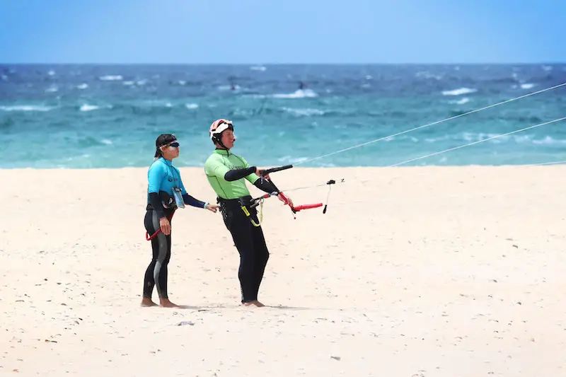 Man learning to fly a kitesurfing kite on the beach in Tarifa while his instructor holds his harness.