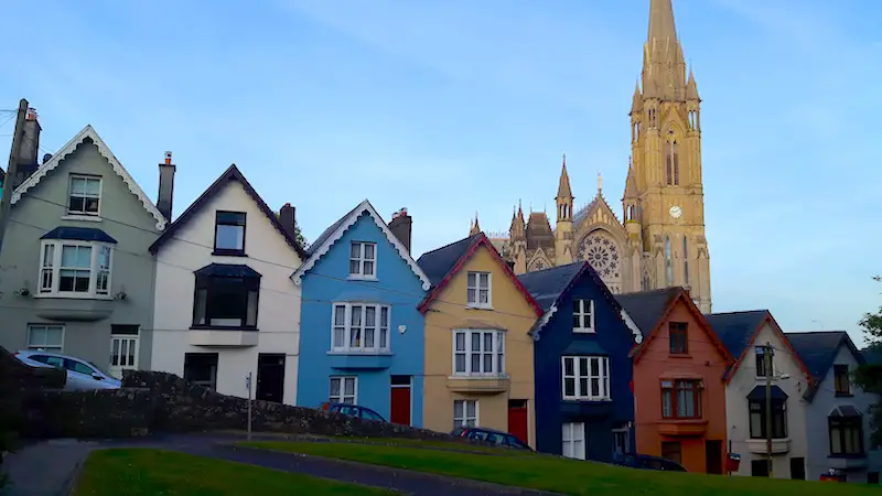 Colourful row of houses in front of a tall church lit by the setting sun in Cobh, Ireland.