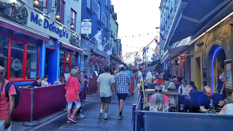 Busy street filled with bar patios on either side in Galway, Ireland.