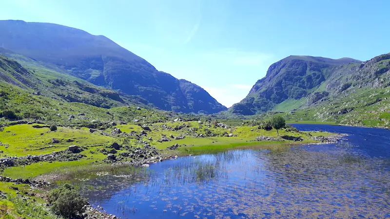 Small lake surrounded by green grass and rugged mountains in the Gap of Dunloe, Killarney, Ireland.
