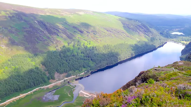 View of long, thin lake surrounded by lush green hills in Glendalough, Ireland.