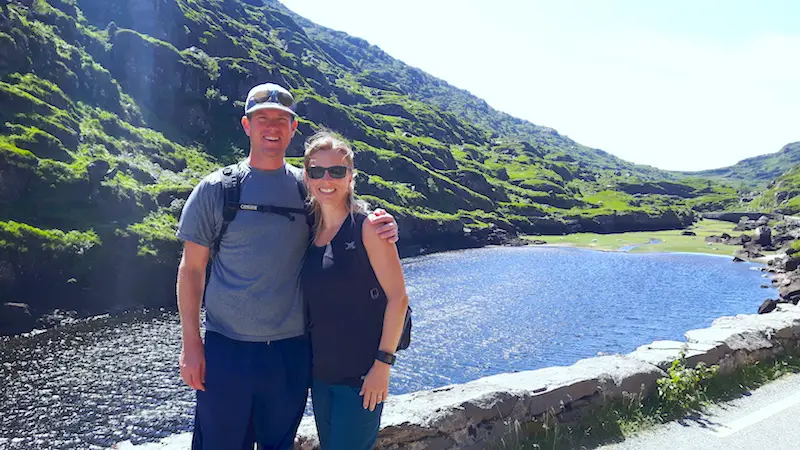 Man and woman in front of a picturesque lake with rock covered hill in Gap of Dunloe, Ireland.