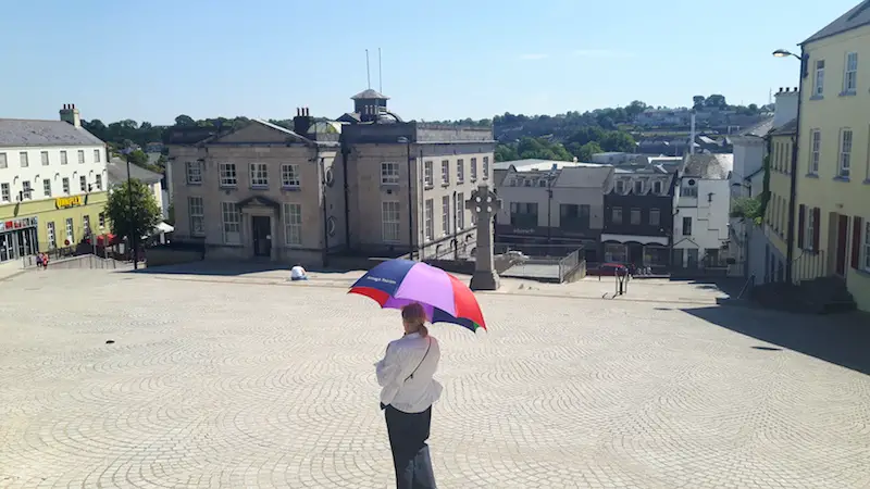 Walking tour guide holding an umbrella in the large open market square of Armagh, Northern Ireland.