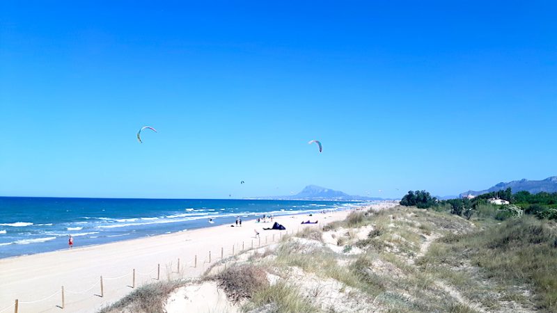 Long sandy beach with mountain in the distance and kites in the sky at Oliva, Spain.