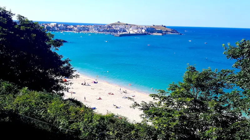 Busy white sand beach with turquoise water between the trees in St. Ives, Cornwall, England.