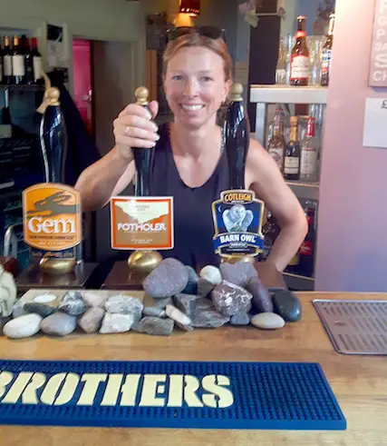 Woman pulling a pint of Potholer beer in Wookey Hole pub, UK.