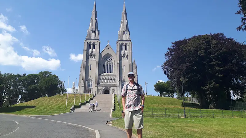 Man standing in front of the grand facade of St Patrick's Catholic Cathedral in Armagh, Northern Ireland.