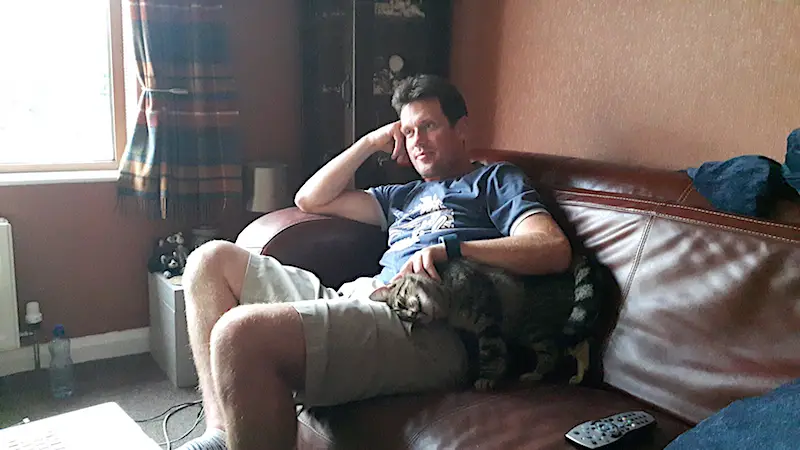Man on a couch with a cat cuddling up while housesitting.