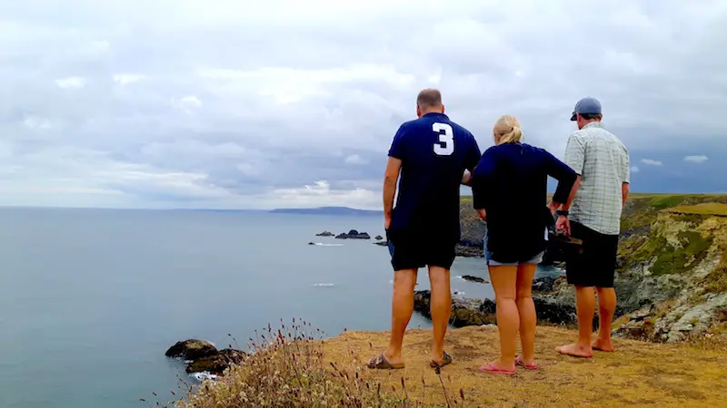 Three people looking over high cliffs for seals on an overcast day in Godrevy, Cornwall.