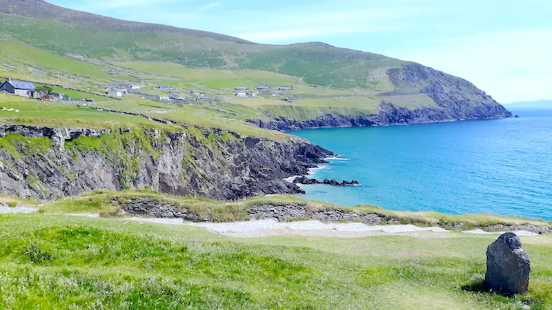 Jagged black cliffs and bright green hills and blue ocean on Slea Head Drive in Dingle, Ireland.