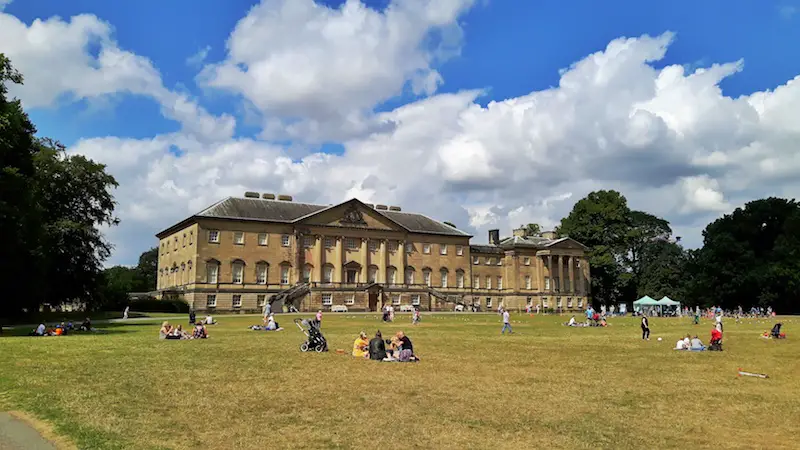 Large stone mansion called Nostell Priory with people relaxing on the grass in front in Yorkshire, UK.