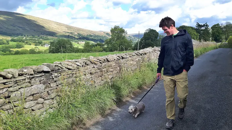 Man walking a small dog down a country lane in the Yorkshire Dales, England.