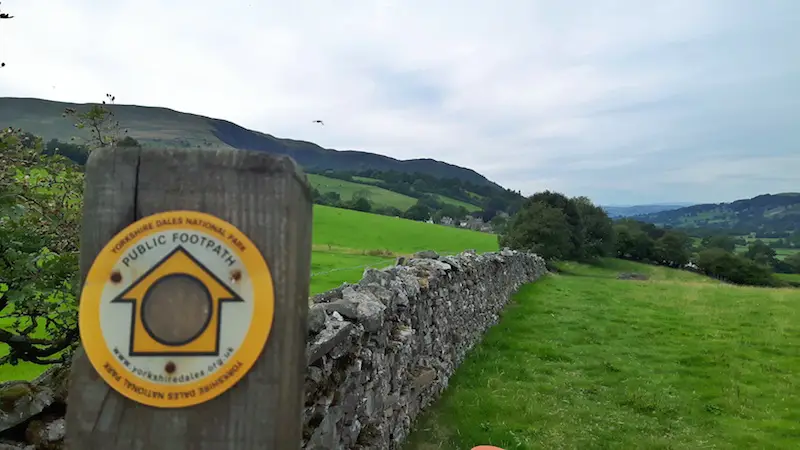 Yellow sign to mark a hiking trail across the Yorkshire Dales attached to a dry stone wall. England.