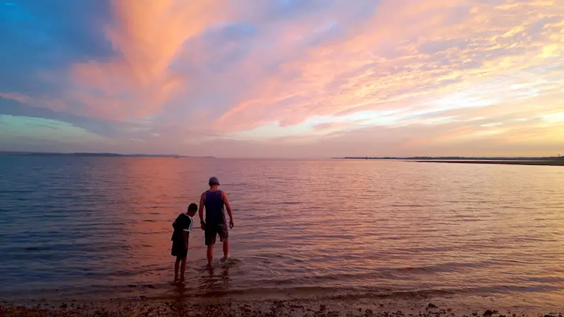 Man and boy paddling in Lepe Beach at sunset, England.