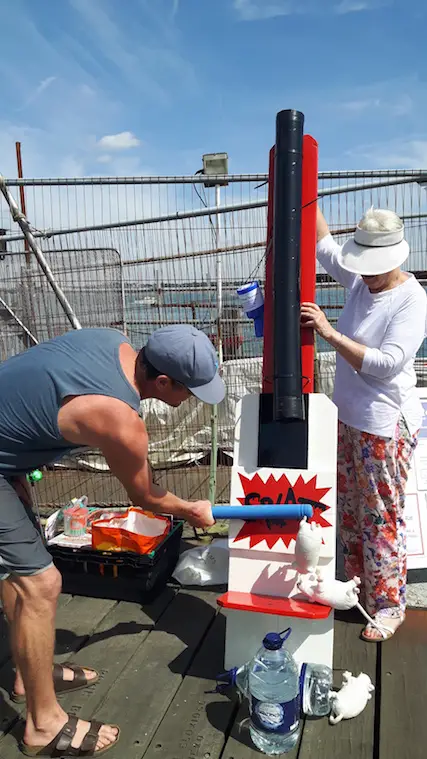 Man trying to splat a rat through a drainpipe at a fairground game in England.