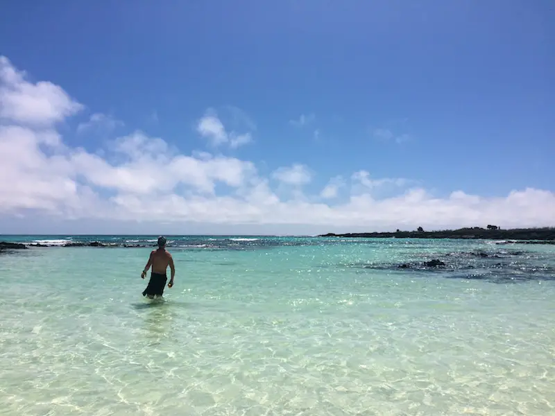 Man wading through shallow water on a crystal clear beach in San Cristobal, Galapagos.