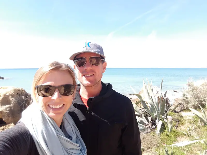 Man and woman on a sunny day with cactus plants and blue ocean behind in the Algarve, Portugal.