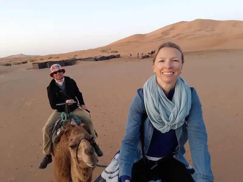 Man and woman riding camels through the Sahara Desert at Merzouga, Morocco.