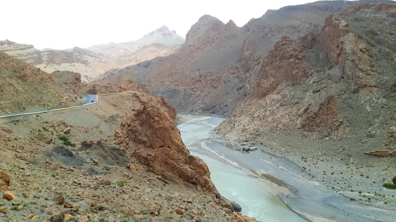 Rugged, rocky scenery with a river running through a valley and a road following it through the Atlas Mountains in Morocco.