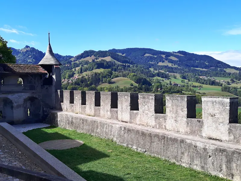 Turreted stone wall with tower at the end in Gruyere overlooking the green hillside, in Switzerland.