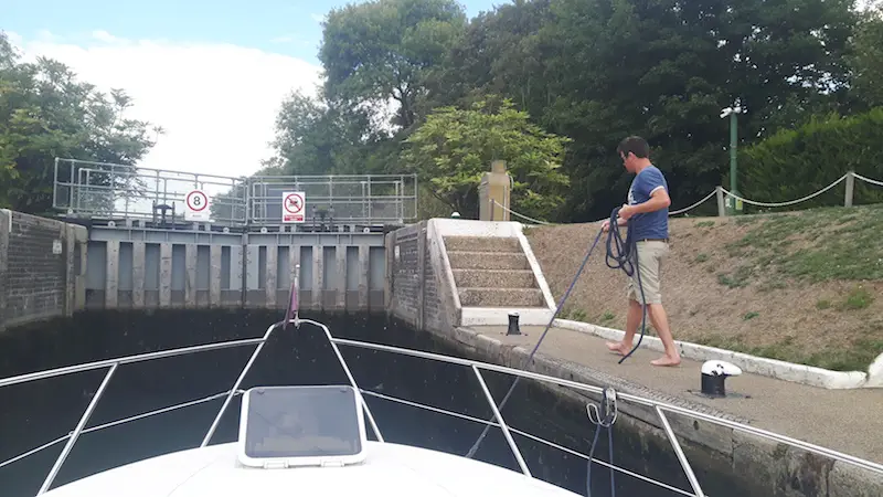 Man holding rope to guide boat through lock gates on River Thames, England.