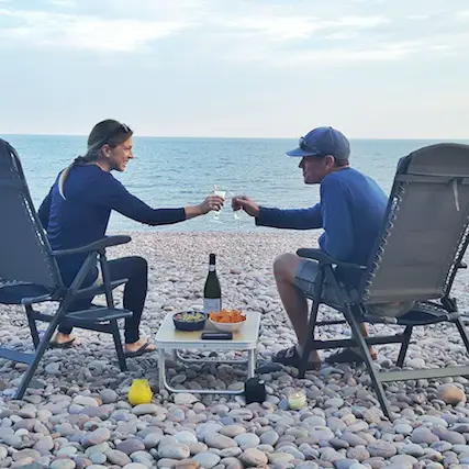 Man and woman with a drink and snacks on a pebble beach in Budleigh Salterton, Devon UK.