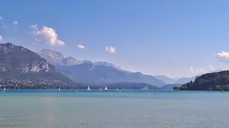 Sail boats in the turquoise waters of Lake Annecy backed by the Alps, France.