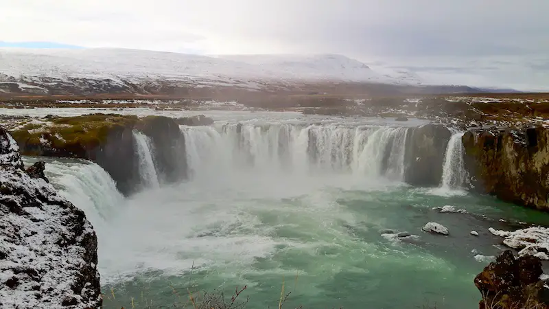 Large horseshoe shaped waterfall crashing into emerald waters at Godafoss Waterfall, Iceland.