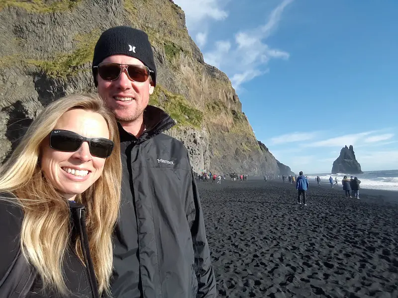 Man and woman on a black sand beach on a sunny day in Iceland.