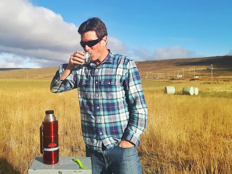 Man drinking soup from a Thermos surrounded by hay fields in Iceland.