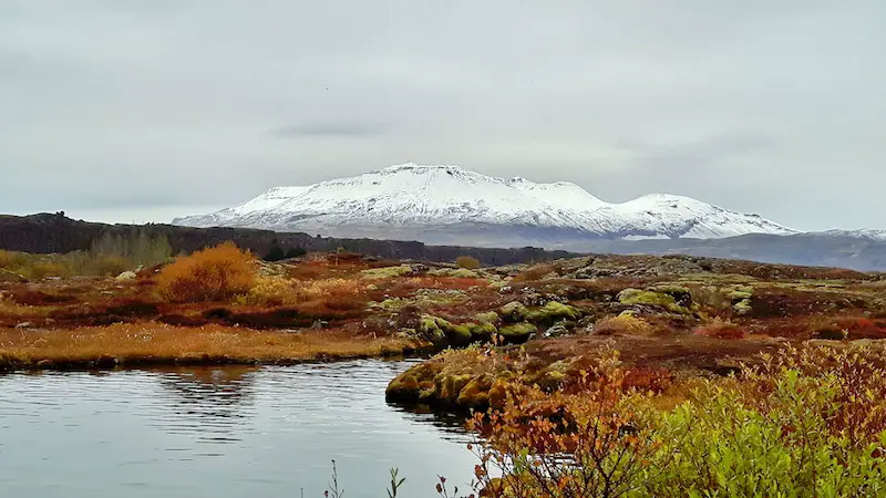 Silfra crack filled with water surrounded by rocky landscapes an a glacier covered mountain in the background in Thingvellir National Park, Iceland.