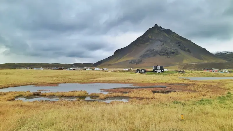 Iceland landscape, ponds, mountain, long grass and dark buildings